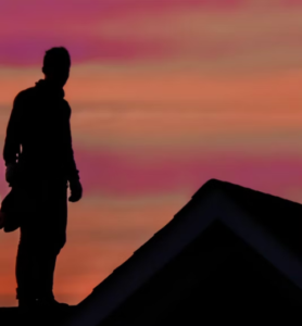 Silhouette of a roofer standing on the roof at sunset