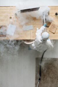 A person wearing PPE fumigating a computer desk