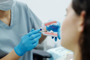 A Person Wearing a Mask and Blue Gloves Showing a Teeth Model to a Patient