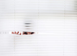 A Person Peeking in White Window Blinds